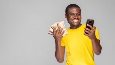 Excited young black man holding money using his phone
